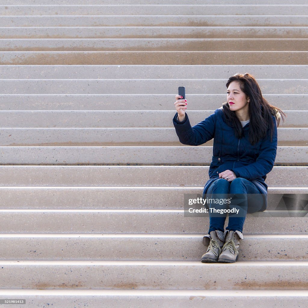 Woman sitting on a step taking a selfie