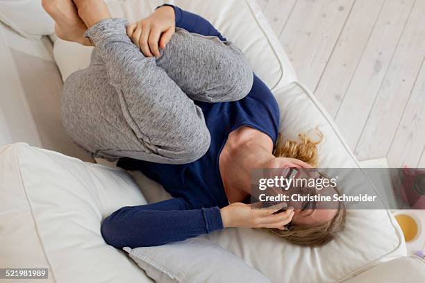 woman lying on sofa laughing on smartphone - tracksuit bottoms stock pictures, royalty-free photos & images