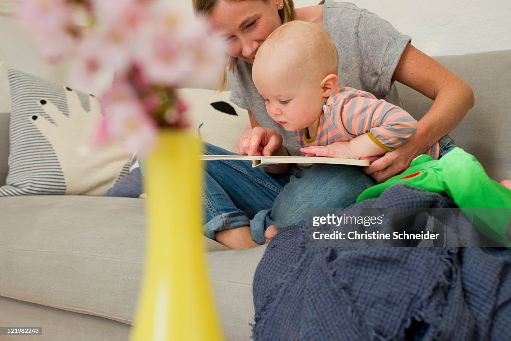 Mature mother reading to baby daughter on sitting room sofa