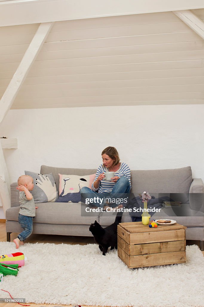 Mature mother drinking coffee with attention seeking baby daughter