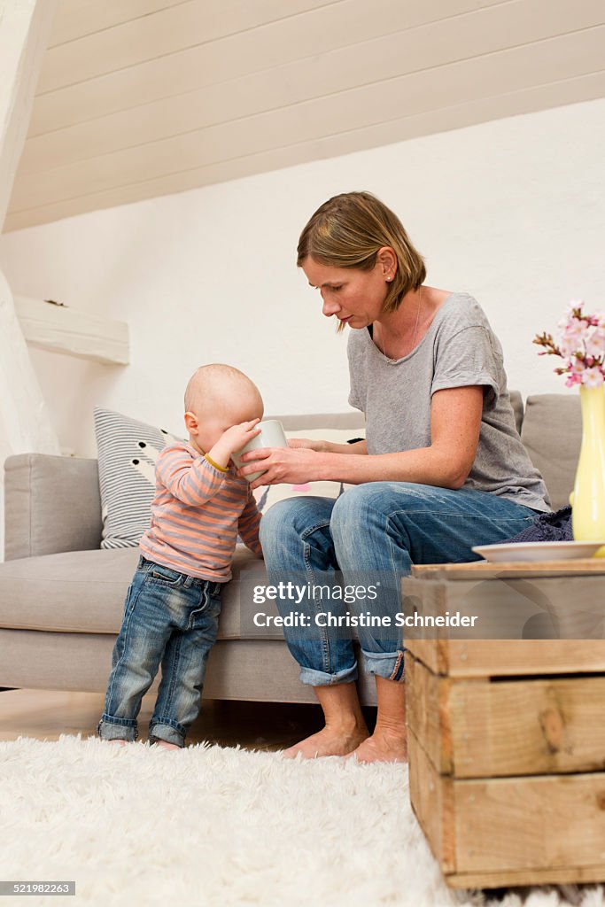 Mature mother sharing drink with baby daughter in sitting room