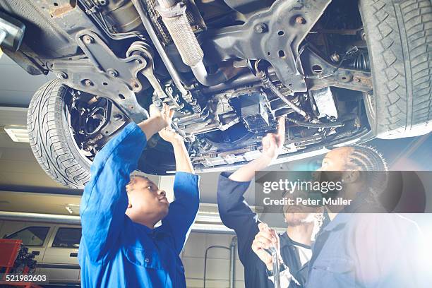 three college students looking up at car in garage workshop - public scrutiny stock pictures, royalty-free photos & images