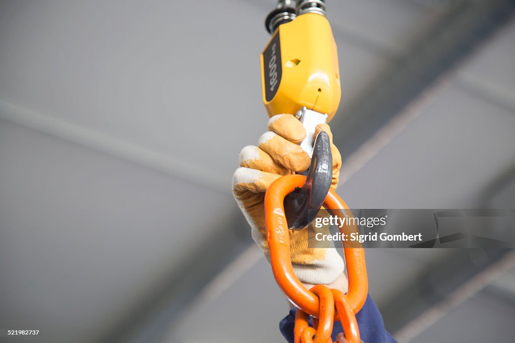 Worker adjusting chain hoist in industrial plant