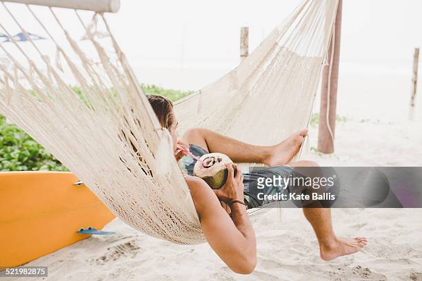 man enjoying coconut water in hammock on beach - legs spread fotografías e imágenes de stock