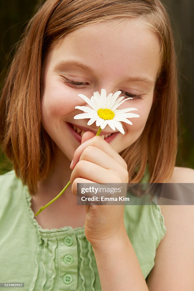 Portrait of girl in garden holding up daisy