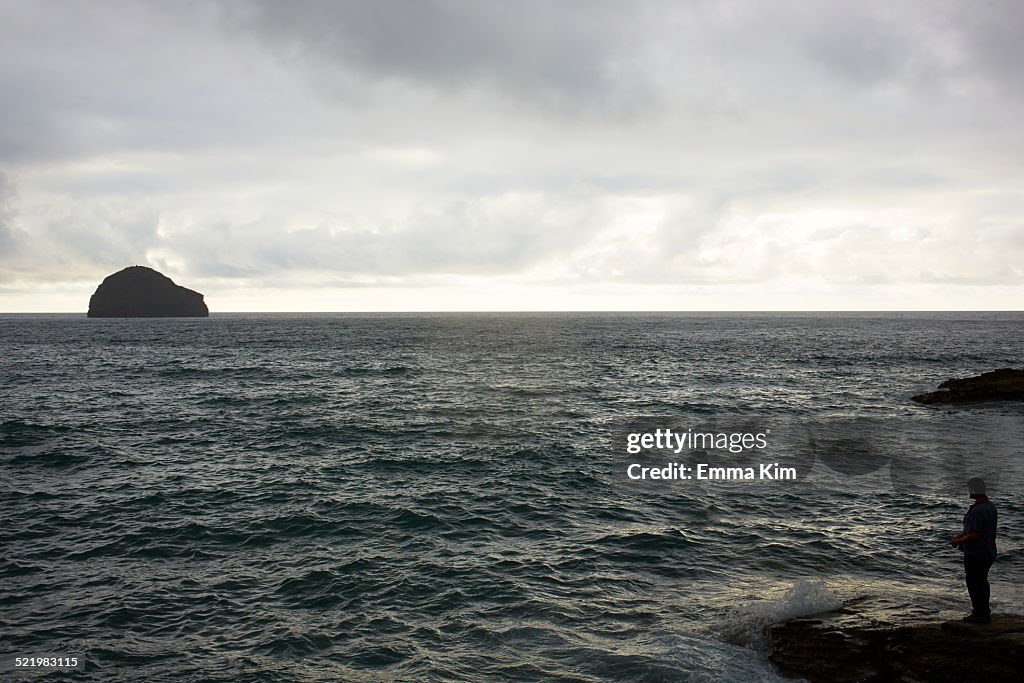 Silhouetted man sea fishing from rock, Treknow, Cornwall, UK