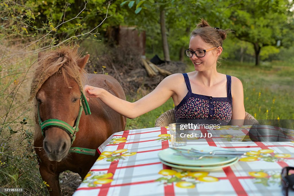 Young woman at table petting pony, Sierra Nevada, Andalucia Granada, Spain