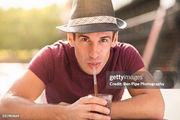 young man wearing hat drinking through straw - sucking fotografías e imágenes de stock