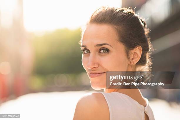 young woman looking over shoulder towards camera - brunette smiling stock pictures, royalty-free photos & images