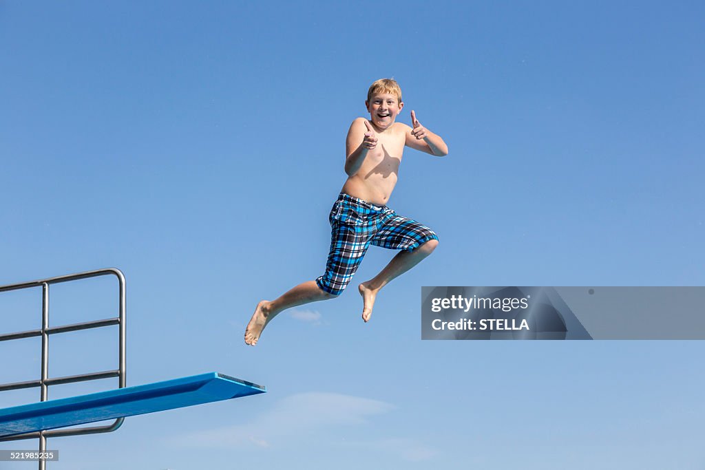 Boy, 10 years, jumping from a three-meter board making a thumbs up gesture