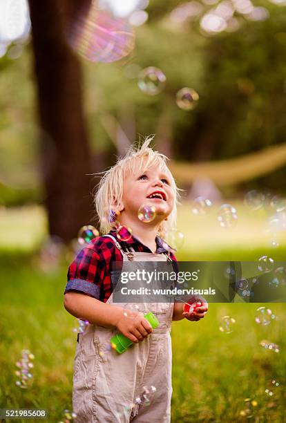 blonde boy getting excited with soap bubbles at the park - toddlers playing outdoor stock pictures, royalty-free photos & images