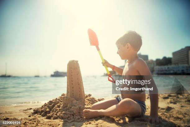 little boy building a sandcastle tower on a beach - sand sculpture stockfoto's en -beelden