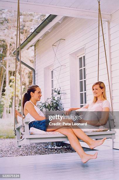 two young women sitting on swing in front of house - swing chair stock pictures, royalty-free photos & images