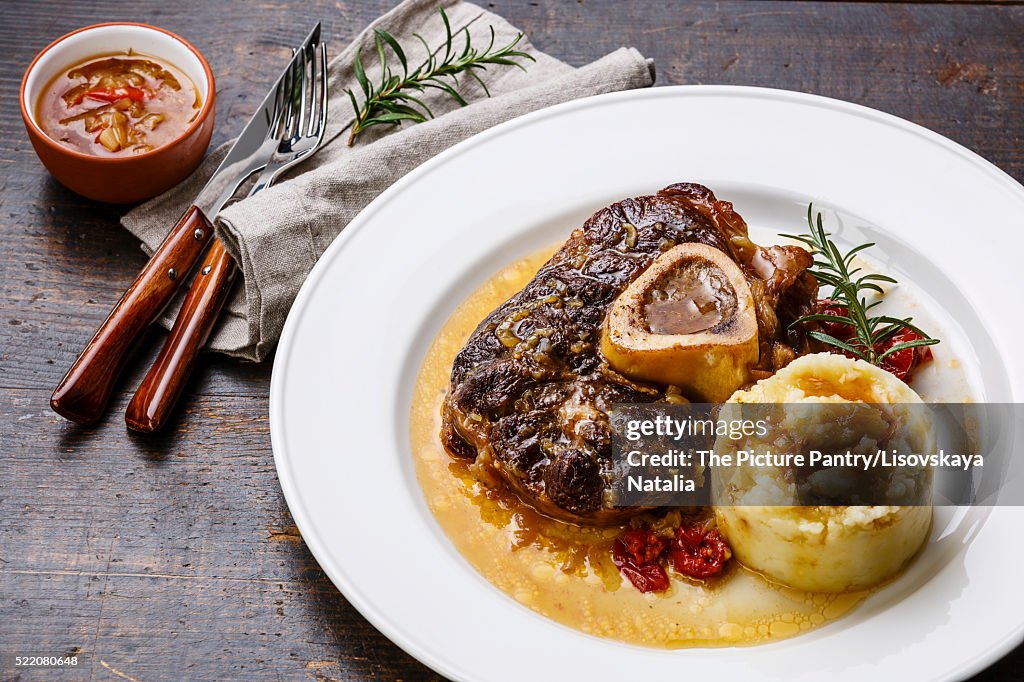 Prepared Osso buco Veal shank with tomatoes and mashed potatoes on white plate on wooden background