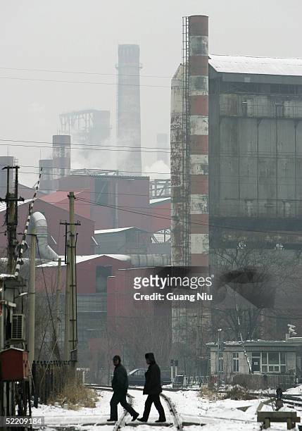 Workers walk past a giant chimney of a power station belching gas on February 17, 2005 in Beijing, China. China, the world's second biggest...