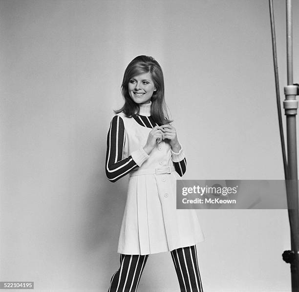 Model Paulene Stone wearing a pleated wool pinafore dress over a striped knitted jumpsuit, 4th March 1969.