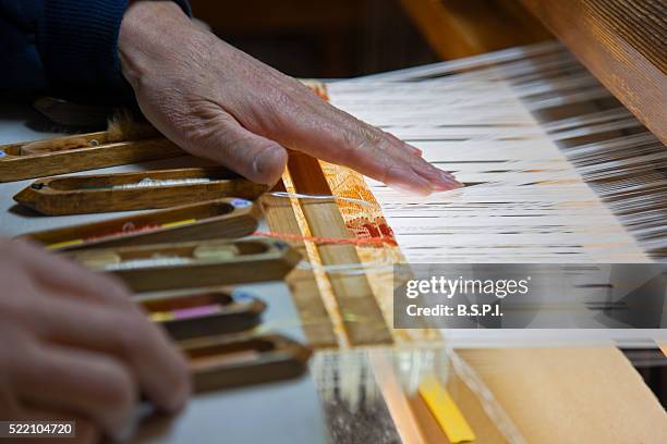 a detailed interior view shows an artisan weaving a silk kimono obi sash on a wooden loom at the kawamura orimono silk weaving workshop (an imperial-family designated weaver), located in the old downtown nishijin weaving district of kyoto, japan. - obi sash fotografías e imágenes de stock