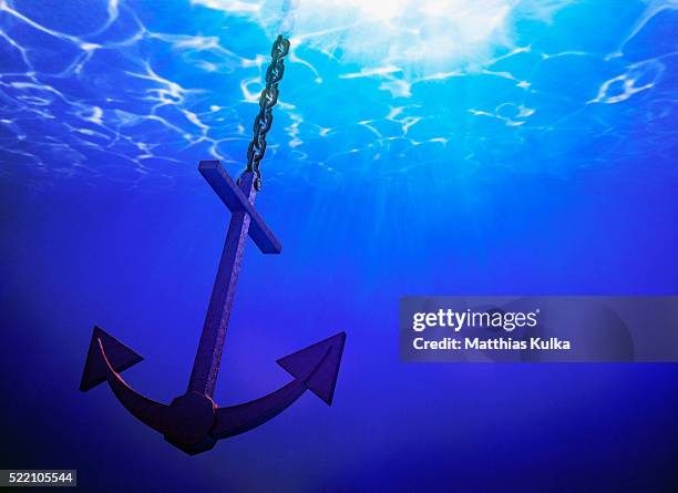 anchor in clear blue sea - anchors stock-fotos und bilder