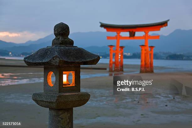 stone lantern and o-torii grand gate at itsukushima shrine on japan's sacred miyajima island - 厳島神社 ストックフォトと画像