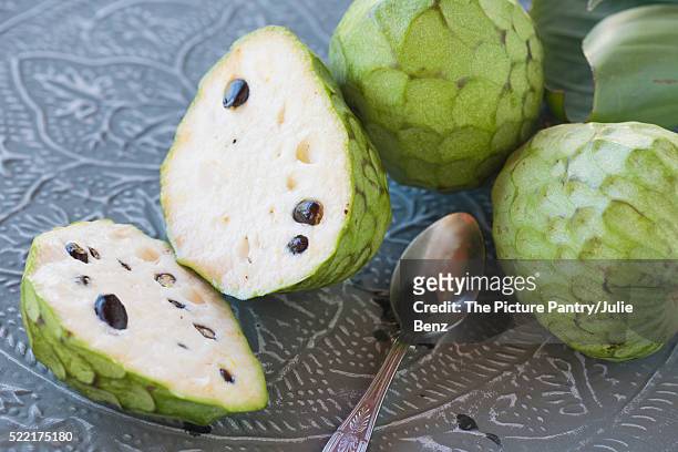 custard fruit on metal tray, whole and cut, with teaspoon - cherimoya stock-fotos und bilder
