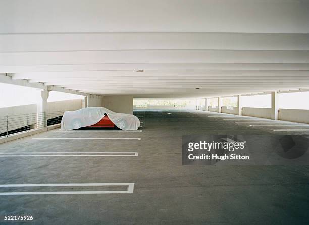 covered red car in empty parking lot - plane stock-fotos und bilder