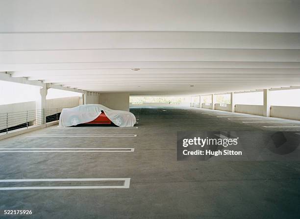 covered red car in empty parking lot - tarpaulin fotografías e imágenes de stock