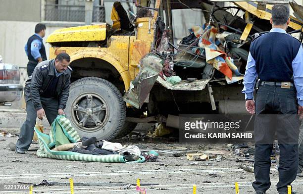An Iraqi policeman wraps a body of an Iraqi with a blanket near wreckage of a destroyed bus 19 February 2005 in Baghdad. The bus was destroyed in a...