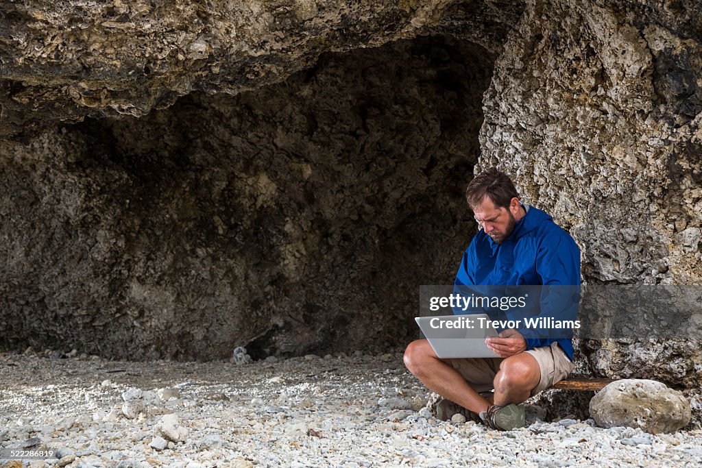 A man using a laptop near a cave opening