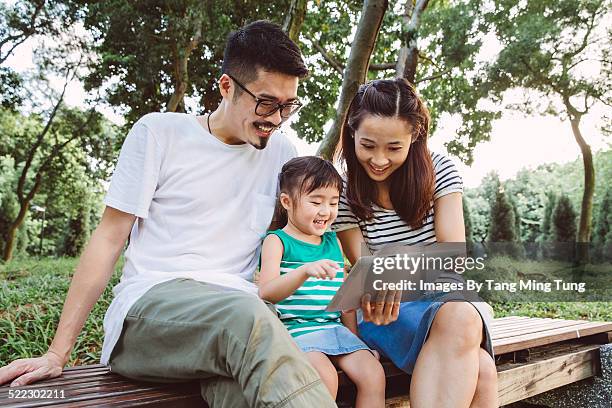 a young happy family using tablet joyfully - in the park day 2 stock pictures, royalty-free photos & images