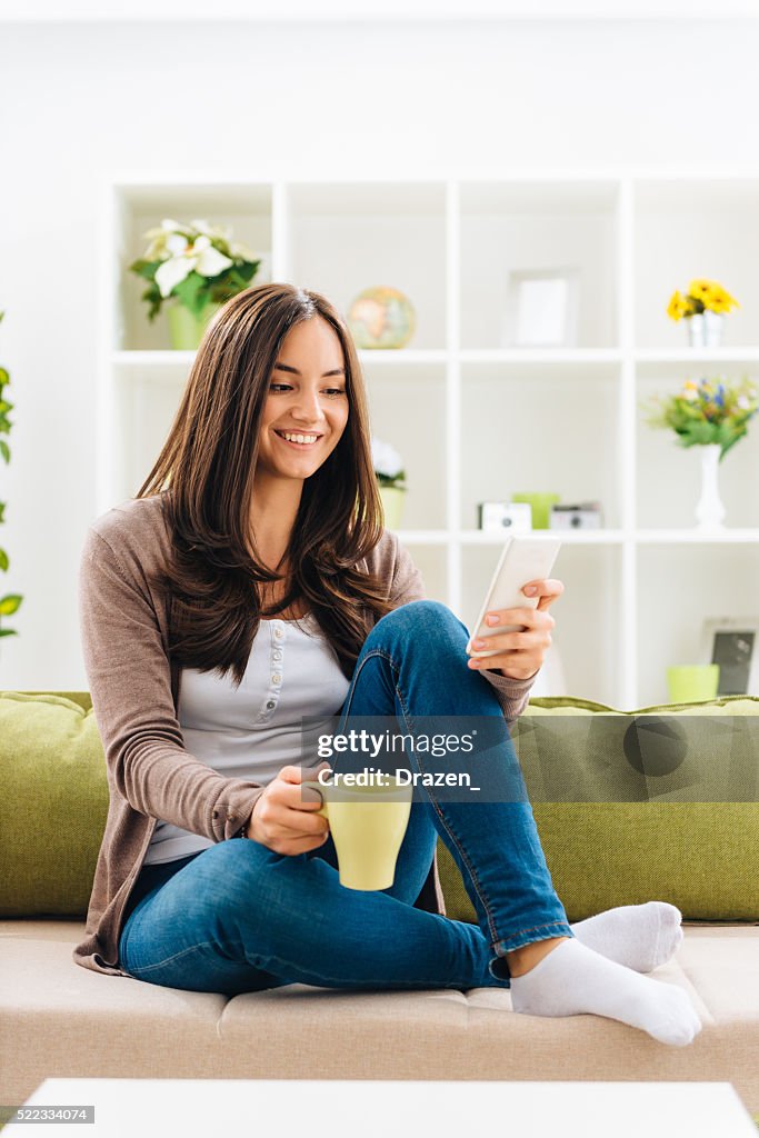 Portrait of cheerful woman drinking coffee and using smartphone