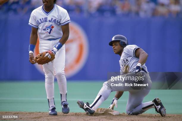 Rickey Henderson of the New York Yankees with one knee on the ground touches second base as he looks on during a game against the Toronto Blue Jays...