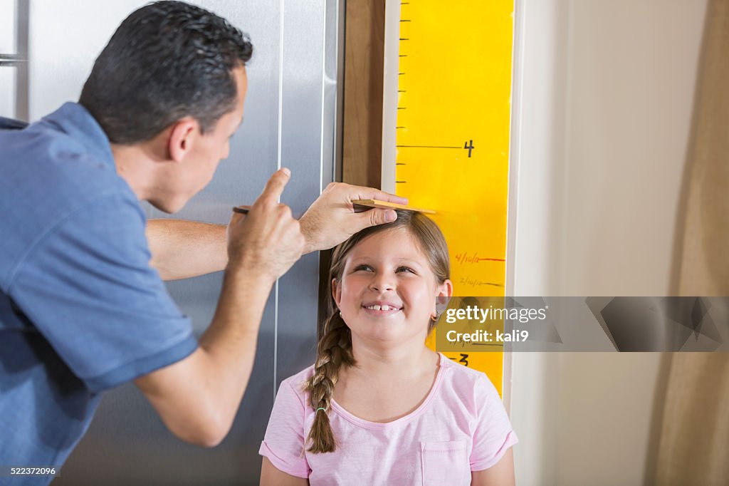 Father measuring girl's height on growth chart