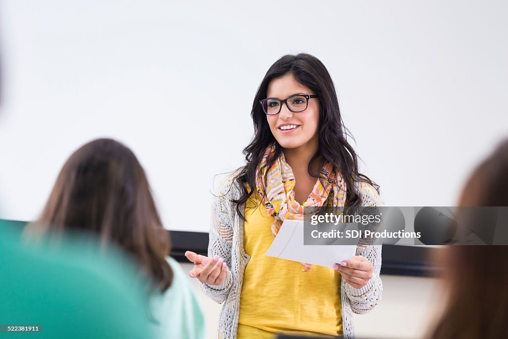 Cute hipster student reading report in front of classmates