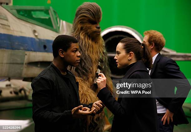 British actors John Boyega and Daisy Ridley speak to each other as Prince Harry talks with Chewbacca in the background during tour of the Star Wars...