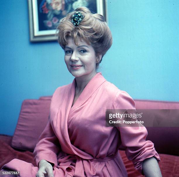 American actress Rita Hayworth wearing a gown whilst sitting on a sofa in London in 1964.