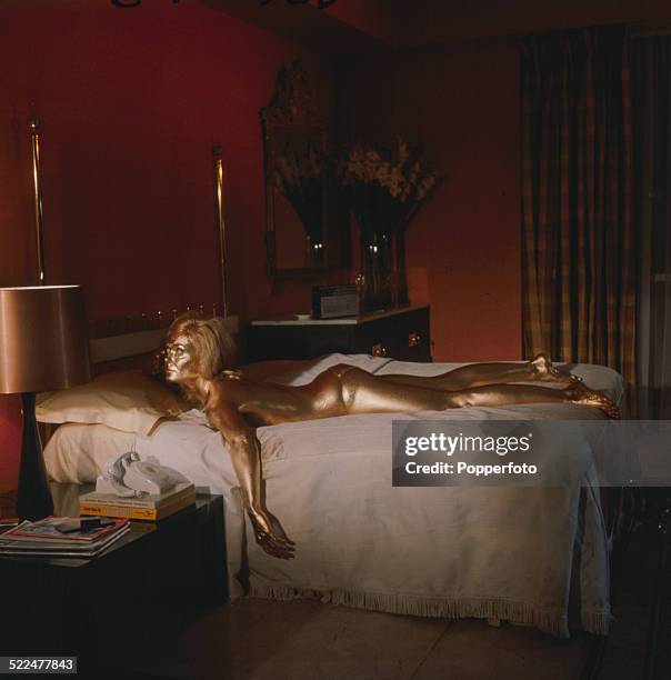 English actress Shirley Eaton pictured in character as Jill Masterson, lying on a bed covered in gold paint in a scene from the James Bond film...