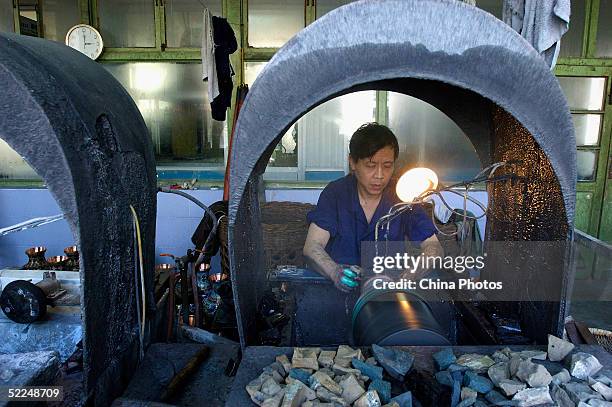 Worker grinds cloisonne wares with emery stones at Beijing Enamel Factory on February 24, 2005 in Beijing, China. Cloisonne enamel was probably...