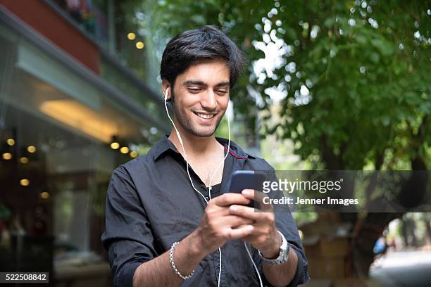 Indian Man standing outdoors with smart phone and earphones.