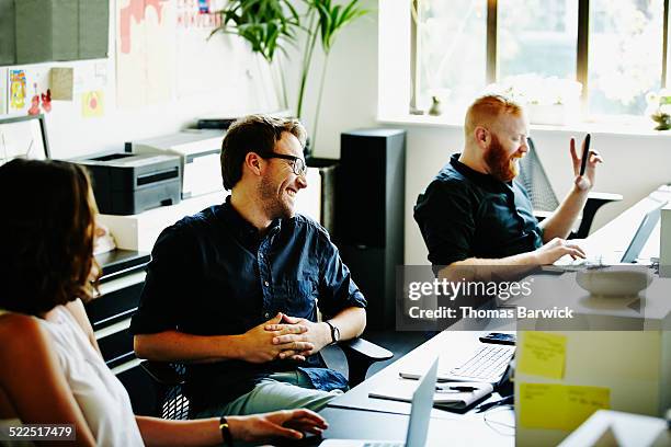 laughing coworkers in office in discussion - grupo pequeño de personas fotografías e imágenes de stock