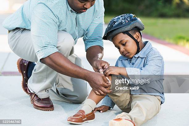 africano american padre poner vendaje en son de la rodilla - leg wound fotografías e imágenes de stock