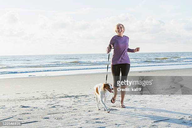 mature woman walking dog on beach - mature adult walking dog stock pictures, royalty-free photos & images