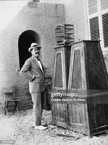 Portrait of British archaeologist Hward Carter as he stands with arms akimbo outside a building next to a cabinet and a birdcage, Egypt, early 1920s.