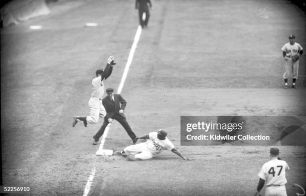 Jackie Robinson of the Brooklyn Dodgers slides into third base ahead of the throw to Gil McDougald of the New York Yankees during a World Series game...