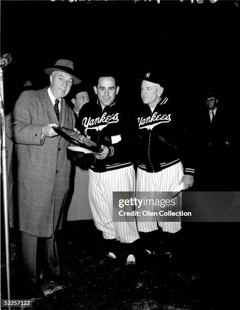 Baseball Commissioner Ford Frick give catcher Yogi Berra his 1955 American League MVP trophy as manager Casey Stengel of the New York Yankees looks...