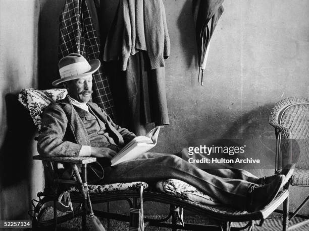 British Egyptology patron George Herbert, Fifth Earl of Carnarvon reclines on a wooden easy chair and reads a book, Egypt, 1923.