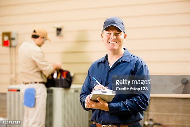 air conditioner repairmen work on home unit. blue collar workers. - installeren stockfoto's en -beelden
