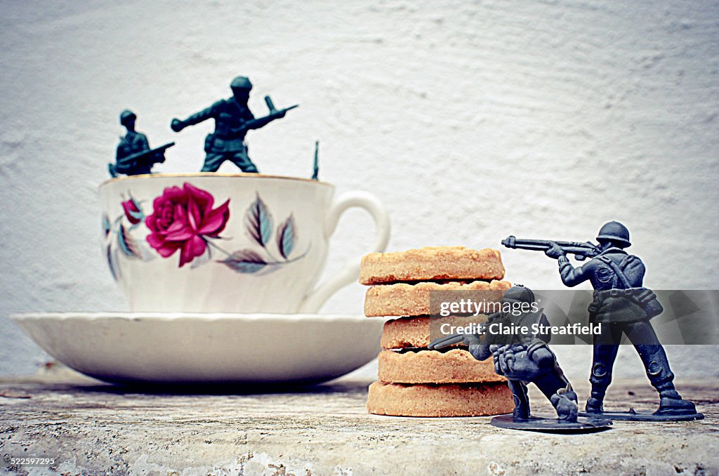 A teacup and biscuits with toy soldiers fighting