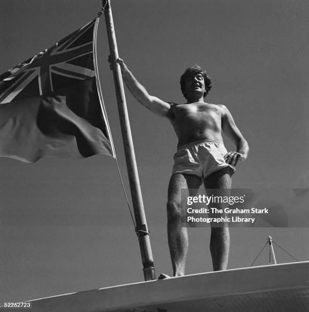 English actor Albert Finney poses with a British ensign flag on a yacht, circa 1969.