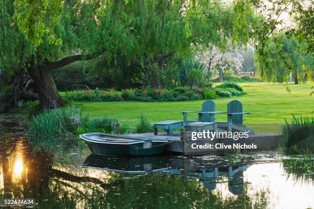 decked terrace beside the lake with adirondack wooden chairs/ seats and boat - chaise adirondack photos et images de collection