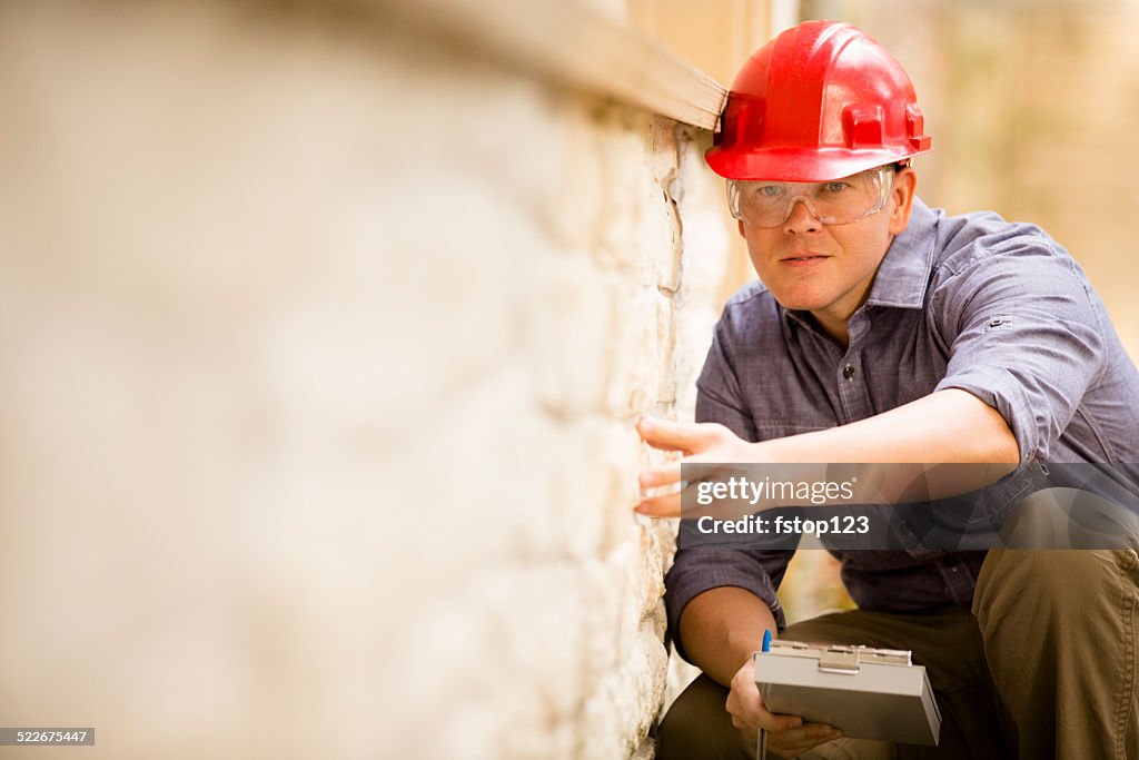 Inspector or blue collar worker examines building wall outdoors.